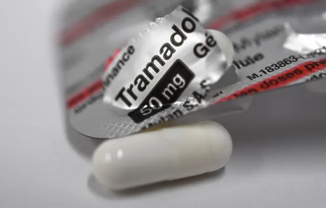 Sebuah pil berwarna putih dengan latar strip obat bertuliskan tramadol.