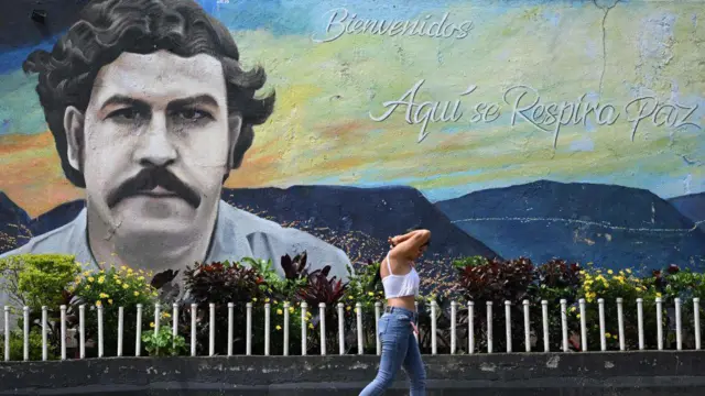 Seorang perempuan berjalan melewati mural dengan wajah Pablo Escobar di kota Medellin, Kolombia