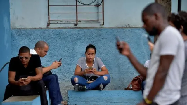Cubanos mirando sus celulares.