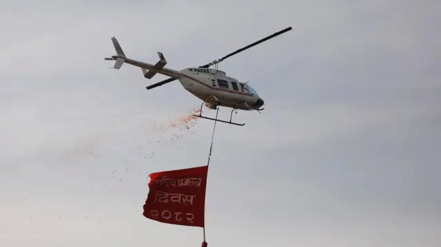 'प्रजातन्त्र दिवस २०८२' लेखिएको एक ब्यानर हेलिकप्टरमा झुन्ड्याएर पुष्पवृष्टि
