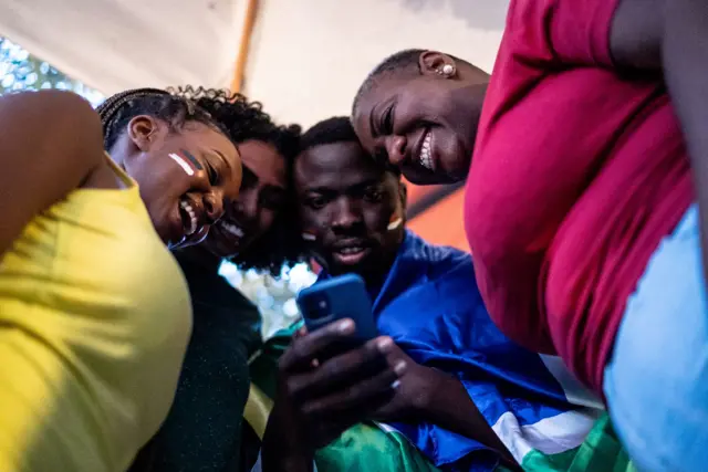 Un homme tenant un téléphone dans ses mains entouré de trois femmes, tous souriant