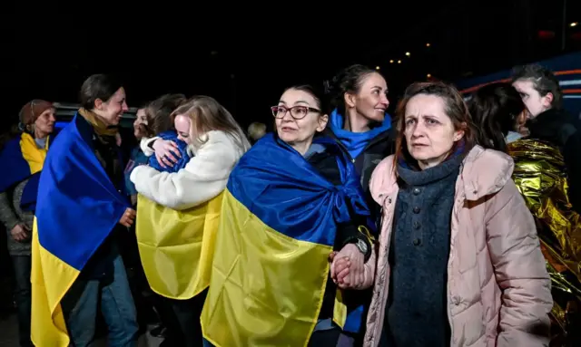 Несколько женщин с украинскими флагами на плечах, несколько - без. Момент прибытия освобожденных украинских узниц 