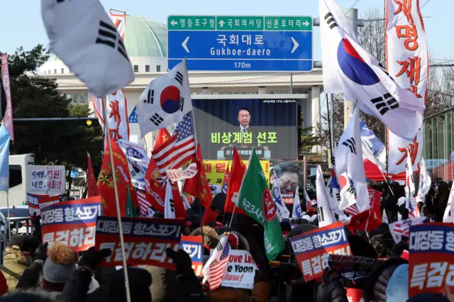 12·3 비상계엄 1년을 맞은 3일 오후 서울 영등포구 여의도 국회의사당역 앞에서 신자유연대 등 보수단체 회원들이 윤석열 전 대통령의 계엄 선포 영상을 지켜보고 있다