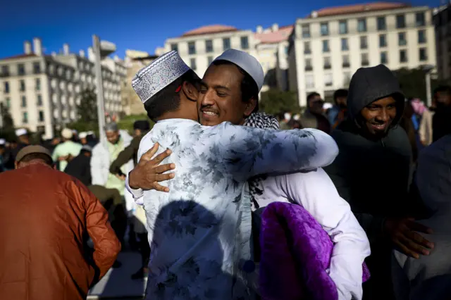 Двое мужчин в исламских шапках улыбаются и обнимают друг друга