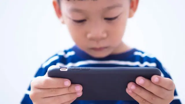 طفل يمسك بهاتف بين يديه ويشاهد فيه أمراً ما