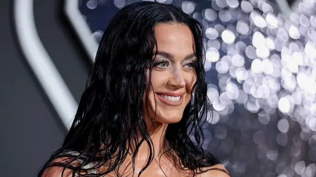 Foto da cantora Katy Perry, uma mulher jovem, de pele e olhos claros, cabelos longos e escuros, que aparece sorrindo.
