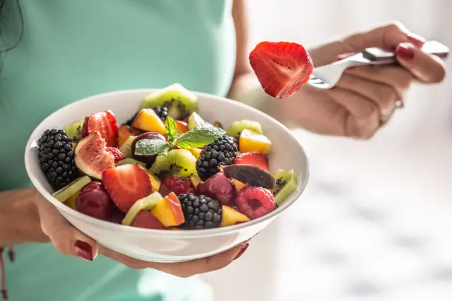 Une femme prend son petit-déjeuner avec une salade de fruits riche en vitamines et en fibres. 