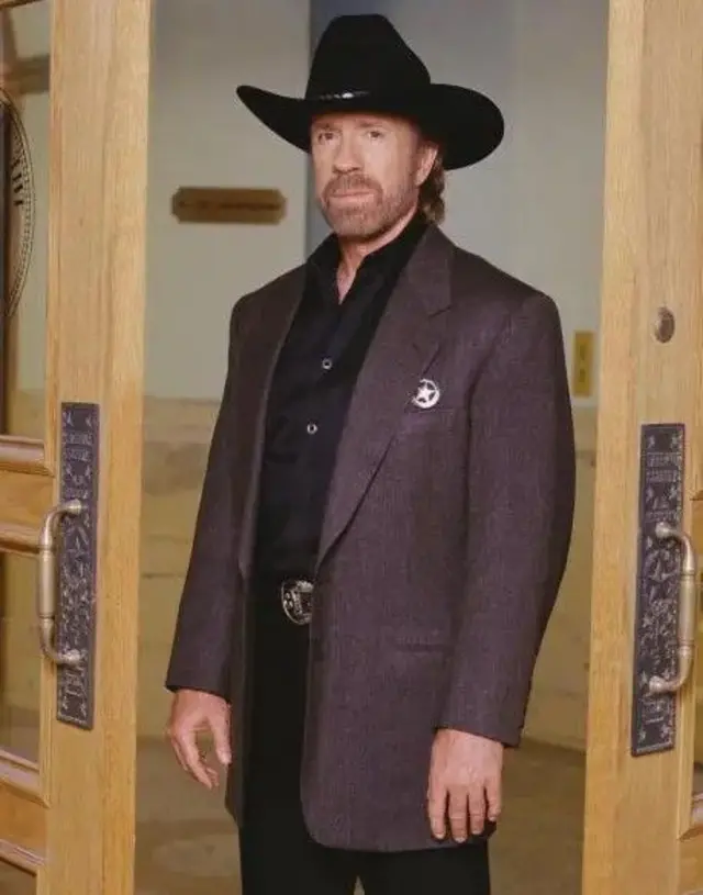 Portrait promotionnel de l'acteur américain Chuck Norris (dans le rôle de Cordell « Cord » Walker), vêtu d'un blazer sur une chemise en satin noir et d'un Stetson noir, posant dans l'embrasure d'une porte pour la série télévisée « Walker, Texas Ranger », 1997.