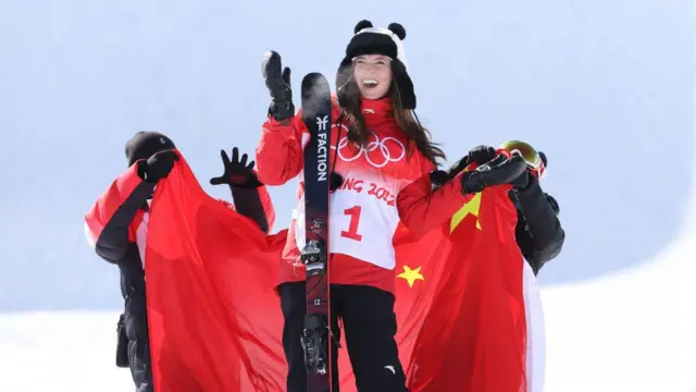 2022年北京冬奥会上，谷爱凌头戴熊猫款式的毡帽，团队人员在身后将中国五星红旗递给她