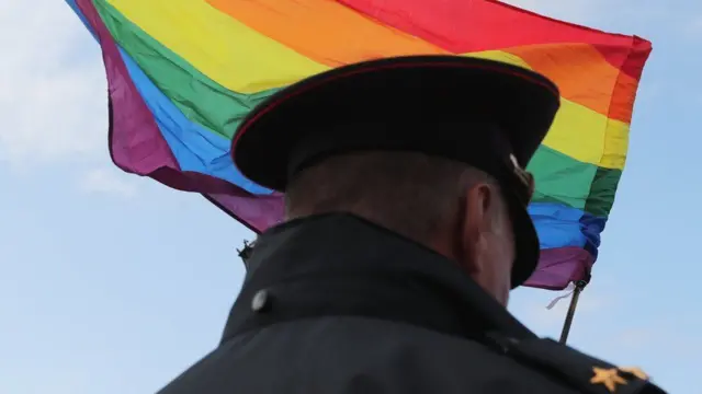 Um oficial russoexcluir conta lampionsbetfrente a uma bandeira do movimento LGBTQIA+