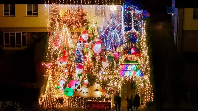 Fotografía de la casa tomada desde arriba con un dron, que muestra luces navideñas amarillas junto a animales inflables.