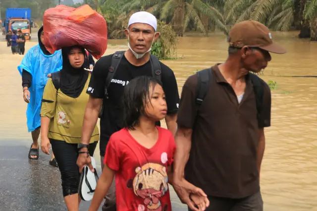 Sejumlah warga korban banjir mengevakuasikan diri ke tempat keluarganya melintasi jalan lintas Nasional Medan-Banda Aceh yang terendam banjir di Desa Sungai Liput, Kecamatan Kejuruan, Aceh Tamiang, Aceh, Selasa (02/12).