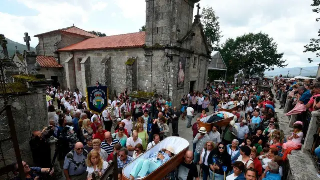 Pessoas levam caixões abertos aos ombros, em frente à igreja de São José de Ribarteme.