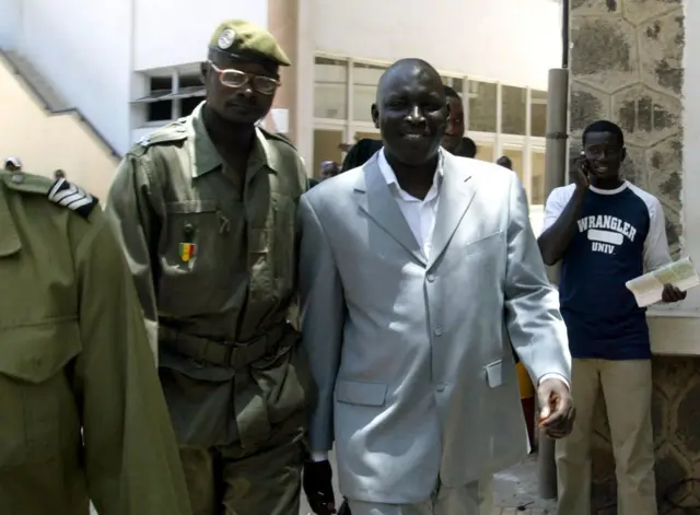 Madiambal Diagne (au centre), escorté par un garde pénitentiaire, quitte le bureau d'un juge à Dakar, le 23 juillet 2004, après une audience de trois heures pour répondre aux accusations de publication de fausses informations dans son journal. 