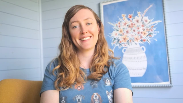 Sian Lawley-Rudd, egy hosszú, szőkésbarna hajú nő mosolyogva ül egy kanapén, mögötte egy virágokat ábrázoló festmény látható egy kékre festett falon. Kék pólót visel, amelyen kutyák vannak.