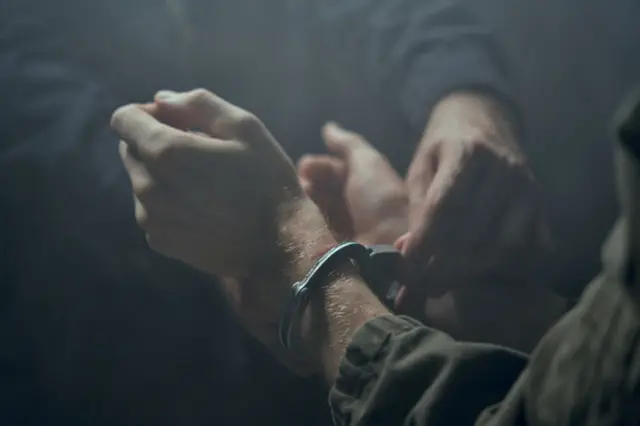 Қоронғи хонада эркак қўлига кишан солишмоқда