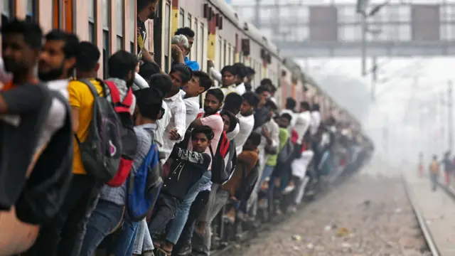 ভারতের একটি ভিড় ট্রেন যেখান থেকে অনেক মানুষ বাইরের দিকে ঝুঁকে আছেন। 