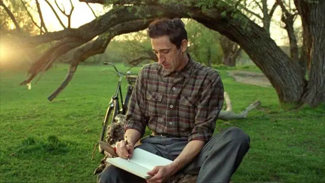 The Brutalist filminden bir sahne: Adrien Brody kırda bir ağaç altında defterine yazarken görülüyor 