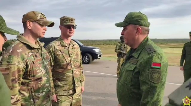 Двоє офіцерів у американській формі, один із них має шеврон із прапором США на плечі, другий – сонцезахисні окуляри. Навпроти – білоруський військовий із прапором Білорусі на плечі