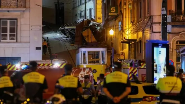 Agentes de policía y equipos de rescate observan el funicular accidentado en una calle empinada de Lisboa durante la noche.