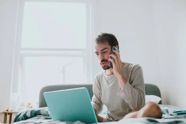 Homem branco segura o celular com caraan space pay pixbetfrustradoan space pay pixbetfrente a um laptop