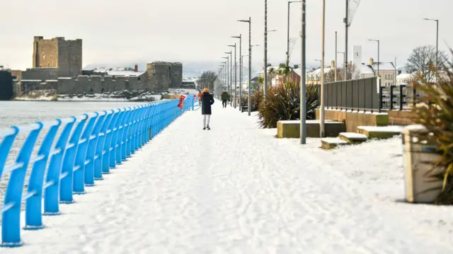 Paisaje invernal de un pueblo con castillo. Se puede ver gente con ropa de invierno caminando por la nieve.