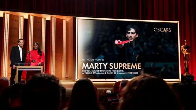 Актеры Даниэль Брукс и Льюис Пуллман объявляют номинаию «Лучший фильм». Сзади них на экране кадр из фильма «Марти Великолепный». Церемония прошла 22 января 2026 года в театре Сэмюэля Голдуина в Беверли‑Хиллз, Калифорния.