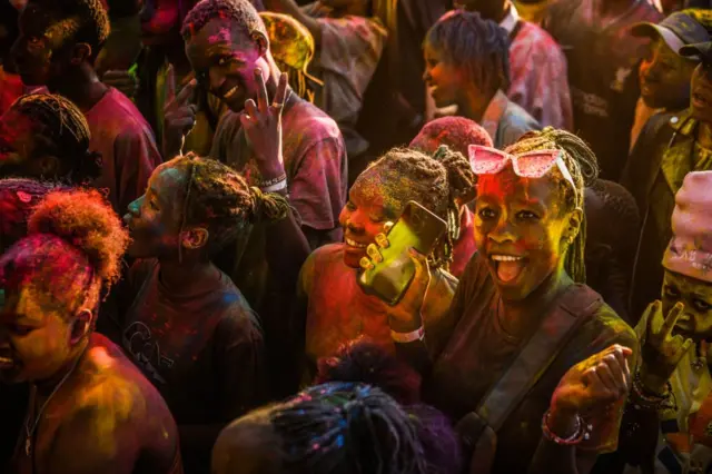 Crowds of smiling people are covered in multicoloured powder.