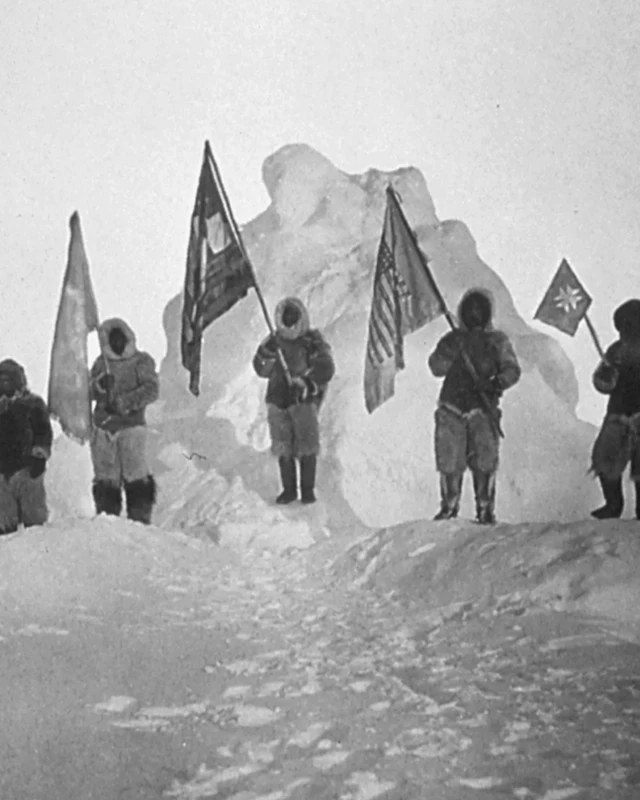 Photo en noir et blanc. Cinq personnes debout dans la neige en tenant chacune un drapeau.
