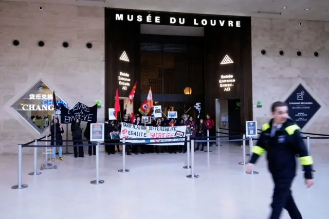 Workers display banners at an entrance of the Louvre museum after they voted to strike for the day over working conditions and other complaints, Monday, Dec. 15, 2025 in Paris