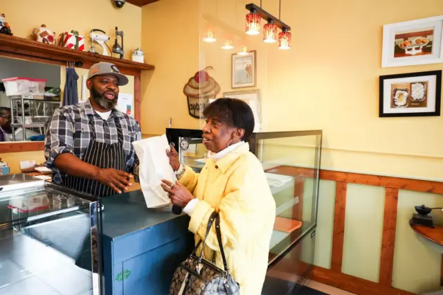 Hunter en la caja de la panadería conversa con una clienta a la que acaba de atender.