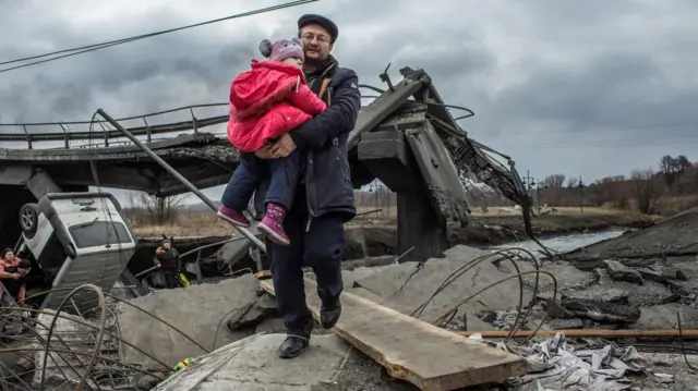 La guerre. Un homme portant un enfant à travers les décombres.