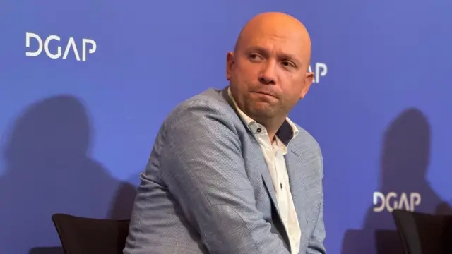 Zaracin u sivom odelu i beloj košulji gleda preko ramena