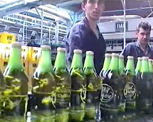Fabrikanın üretim bantında çekilmiş bir fotoğraf. Şişeler ve işçiler görünüyor. 