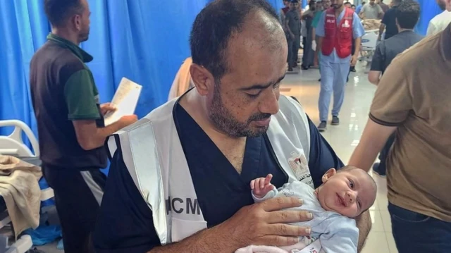 Dr Muhammad Abu Salamiya holding a baby in a bustling hospital ward