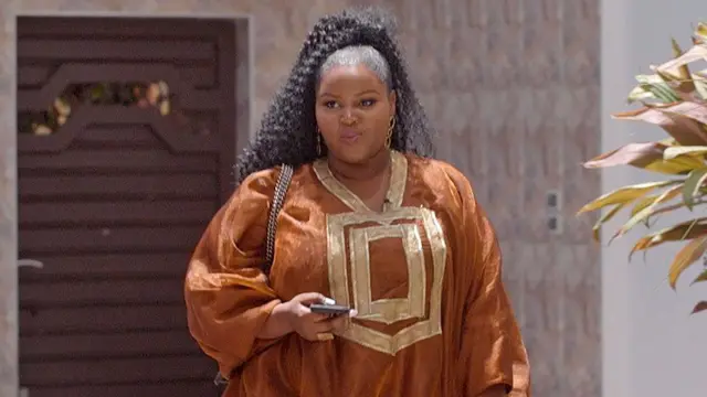 Salamata Konte yambaye umwambaro w'ikanzu y'amaboko maremare izwi nka 'boubou', mu kiganza kimwe afite telefone igendanwa. Afite imisatsi miremire idefurije 