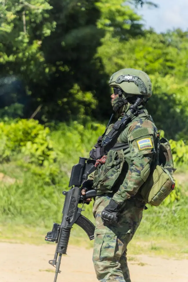 Umusirikare w'u Rwanda wo mu mutwe wo kurwanya iterabwoba, ari ku burinzi mu mujyi wa Mocimboa da Praia, mu majyaruguru ya Mozambique, ku itariki ya 16 Kuboza (12) mu 2023. Yambaye impuzankano za gisirikare, ahetse agakapo mu mugongo, ukuboko kw'iburyo gufashe imbunda kuyirebesha hasi. Yambaye n'ingofero ikomeye ya 'casque', n'indorerwamo z'izuba. Hirya ye hari ibyatsi n'ibiti bitohagiye. 