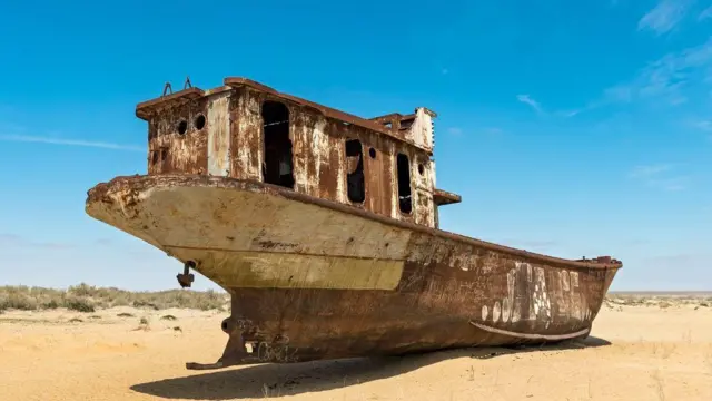 Embarcação encalhada na areia e enferrujada onde antes foi o Mar de Aral, transformado em uma região árida