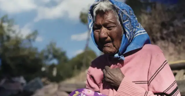 Rita Patino dans son village natal, frêle et très âgée. Elle s'est également recouvert la tête d'un foulard bleu.