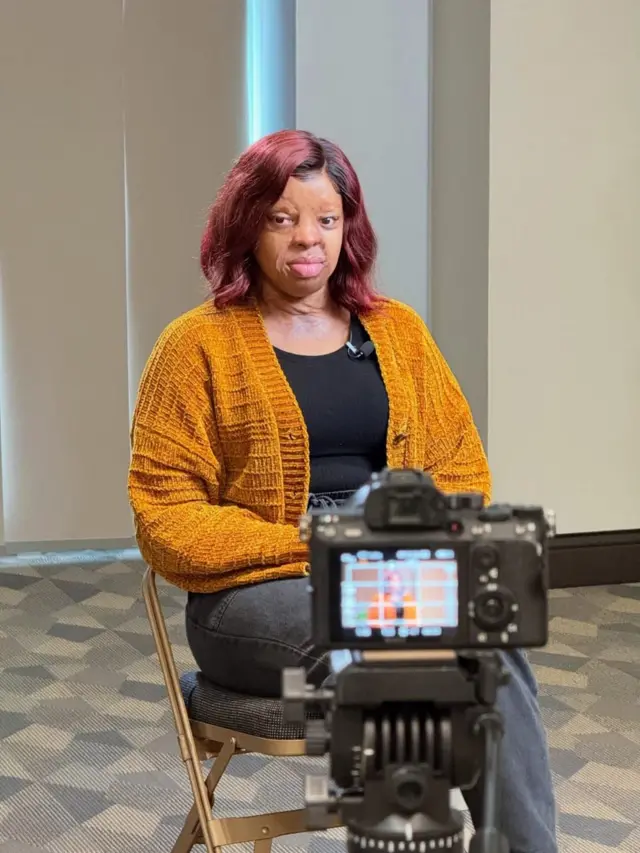 Ikechi wear brown sweater with black stripes in bugler Sidon dey look camera