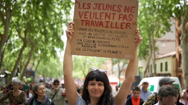 Девојка држи транспарент са поруком: Млади не желе више да раде за малу плату, капитализам и неоколонијални систем без права на пензију и бенефиције