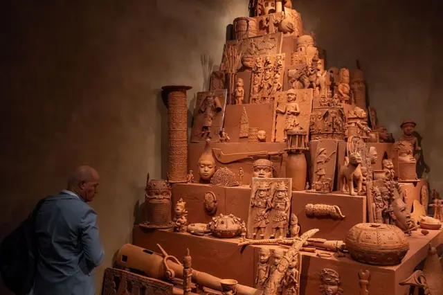 Une personne contemplant le Monument à la restitution de l'esprit et de l'âme de Yinka Shonibare – une structure pyramidale composée de plus de 150 répliques en argile des bronzes du Bénin.