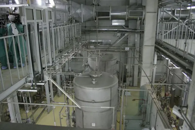 یک کارمند امنیتی ایرانی قبل از ورود محمد خاتمی، رئیس‌جمهور ایران، در خارج از شهر اصفهان، در ۴۱۰ کیلومتری جنوب پایتخت تهران، در بخشی از تأسیسات تبدیل اورانیوم قدم می‌زند. تاسیسات تبدیل اصفهان کنسانتره سنگ اورانیوم موسوم به کیک زرد را دوباره به گاز هگزافلوراید اورانیوم فرآوری می‌کند. سپس گاز به نطنز برده می‌شود و برای غنی‌سازی وارد سانتریفیوژها می‌شود