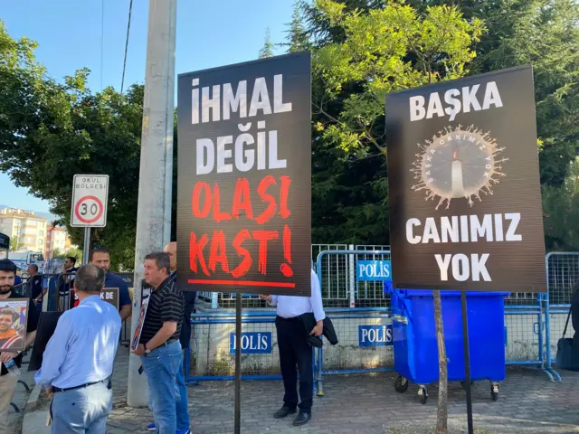 Üzerinde "İhmal değil olası kast!" ve "Başka canımız yok" yazan iki döviz.