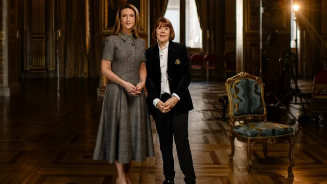 İki çok iyi giyimli kadın ayakta poz veriyorlar, bulundukları oda çok geniş ve eski dönemlerden kalma mobilyalar var. Bir saray izlenimi veriyor.