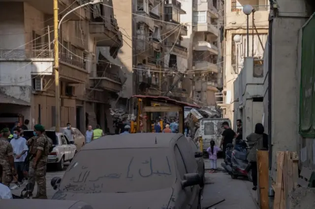 Edifícios e pessoas em Basta, bairro de Beirute, além do carro coberto de poeira com mensagem elogiando líder do Hezbollah