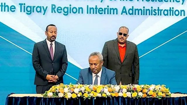 አዲሱ የትግራይ ክልል ጊዜያዊ አስተዳደር ፕሬዝዳንት ጄነራል ታደሰ ወረደ ፊርማቸው ሲያኖሩ። ከጀርባቸው ጠቅላይ ሚኒስትር ዐቢይ እና የቀድው ፕሬዝዳንት አቶ ጌታቸው ረዳ ቆመው።