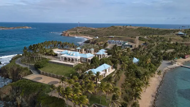 Aerial view of Little St James island there is a large estate with multiple buildings, palm trees, and blue-roofed villas surrounded by the sea.