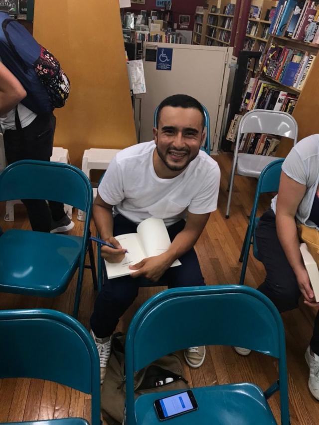 Zamora sentadosportsbet ao vivouma carteira, sorrindo, enquanto assina um livro