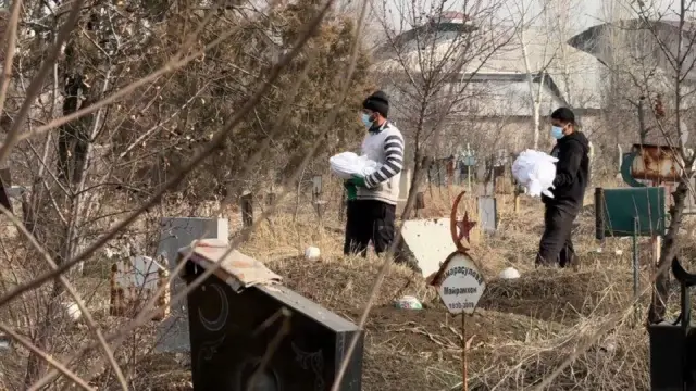 Қабристон. Оқ матога ўралган суякларни кўтариб кетаётган икки киши